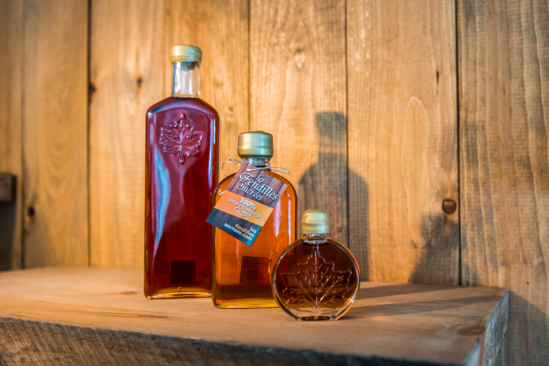 Bouteilles de sirop d’érable artisanal présentées sur une tablette en bois, une spécialité locale de Chalets Lanaudière.