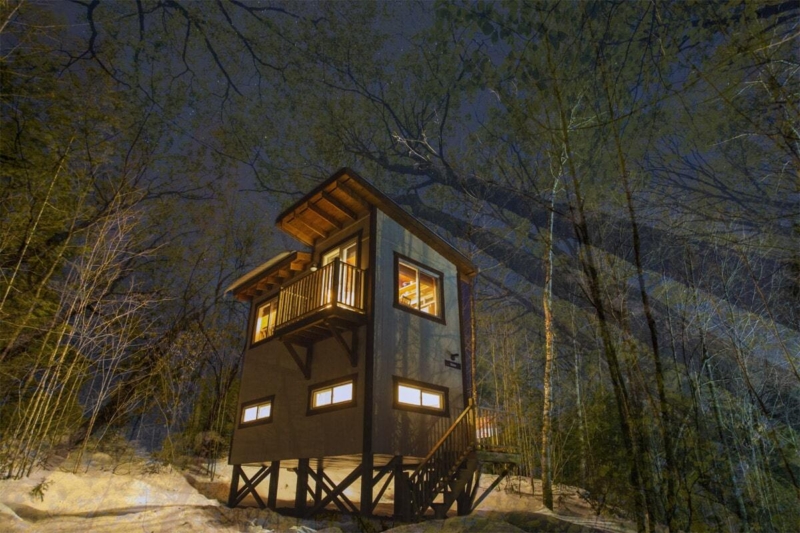 Chalet sur pilotis éclairé la nuit, entouré d’arbres et de neige, dans la forêt de Chalets Lanaudière.