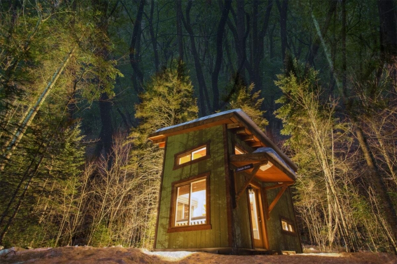 Petit chalet en bois de Chalets Lanaudière niché au cœur d’une forêt, éclairé par la lumière dorée du soleil.