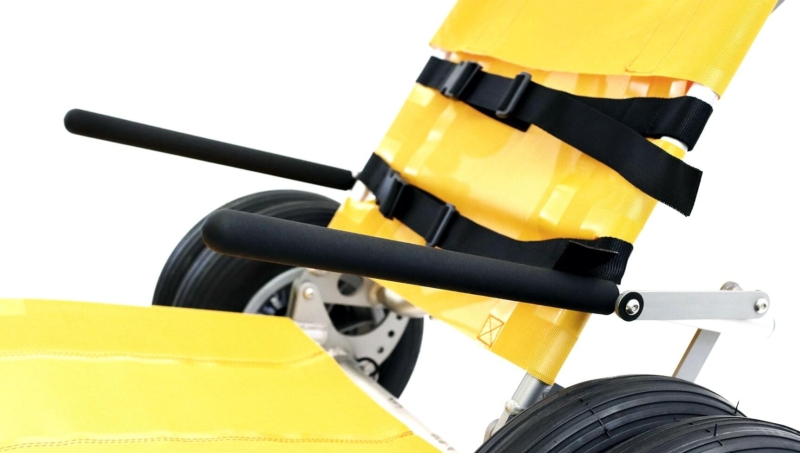 Gros plan sur une chaise roulante tout-terrain jaune, un équipement adapté aux activités de plein air près des chalets.