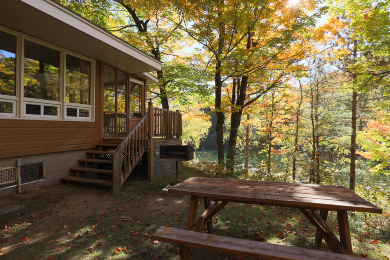Cottage de Chalets Lanaudière en forêt, avec terrasse, table de pique-nique et vue sur un lac.
