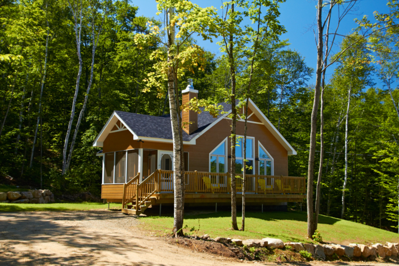 Chalet en bois de Chalets Lanaudière entouré d’arbres, avec grande terrasse, terrain gazonné et entrée en gravier.