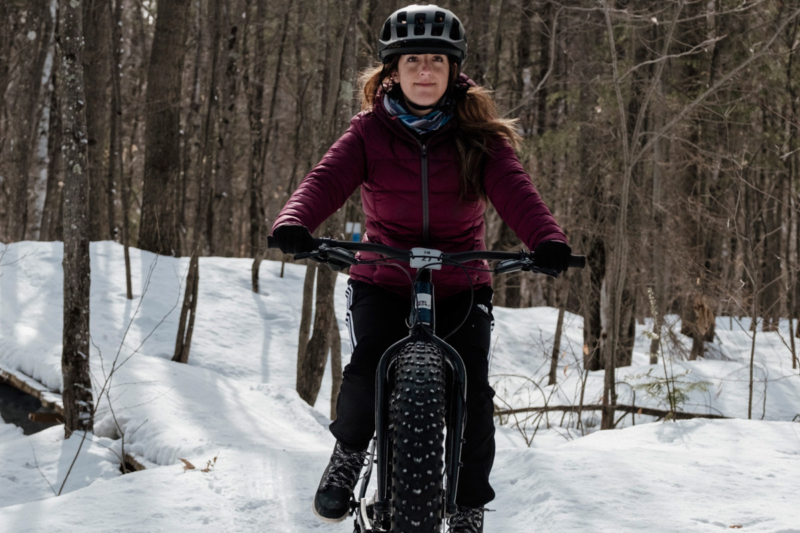 Personne à vélo à pneus surdimensionnés parcourant un sentier enneigé en forêt près d’un chalet de Chalets Lanaudière.