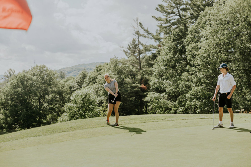 Deux personnes jouent au golf sur un vert entouré d’arbres et de collines, près des chalets de Chalets Lanaudière.