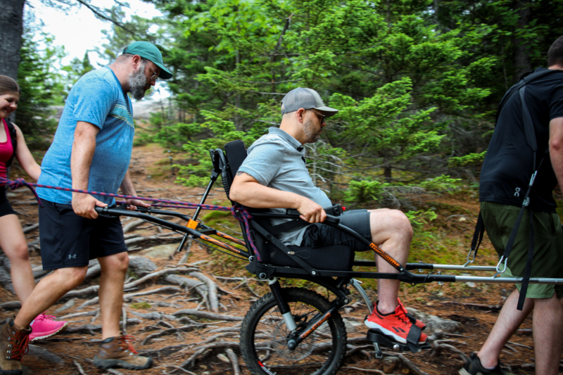 Groupe en randonnée adaptée dans la forêt près des chalets de Chalets Lanaudière, avec une personne en fauteuil tout-terrain.
