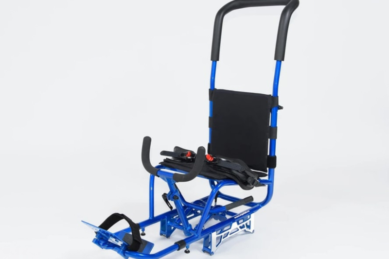 Chaise roulante tout-terrain bleue avec grandes poignées, repose-pieds et harnais, conçue pour faciliter les déplacements en plein air.