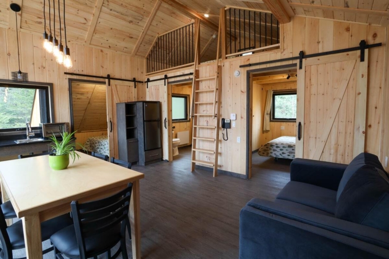 Intérieur chaleureux d’un chalet en bois avec cuisine, salle à manger, salon, mezzanine et chambre à coucher.