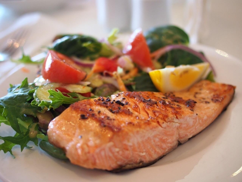 Filet de saumon grillé servi avec une salade fraîche, des tomates et un quartier de citron.
