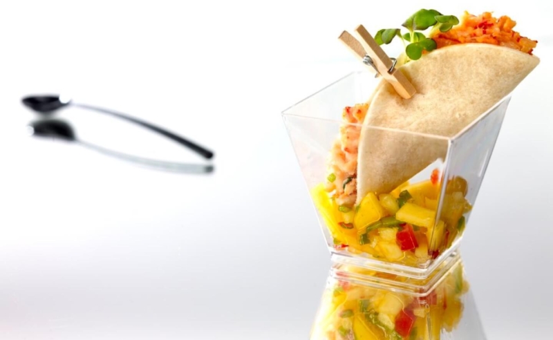 Taco coloré accompagné de légumes frais, présenté dans un verre élégant avec pinces décoratives.