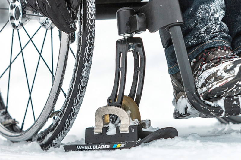 Gros plan sur une roue de fauteuil roulant et une lame de ski adaptée pour se déplacer dans la neige.