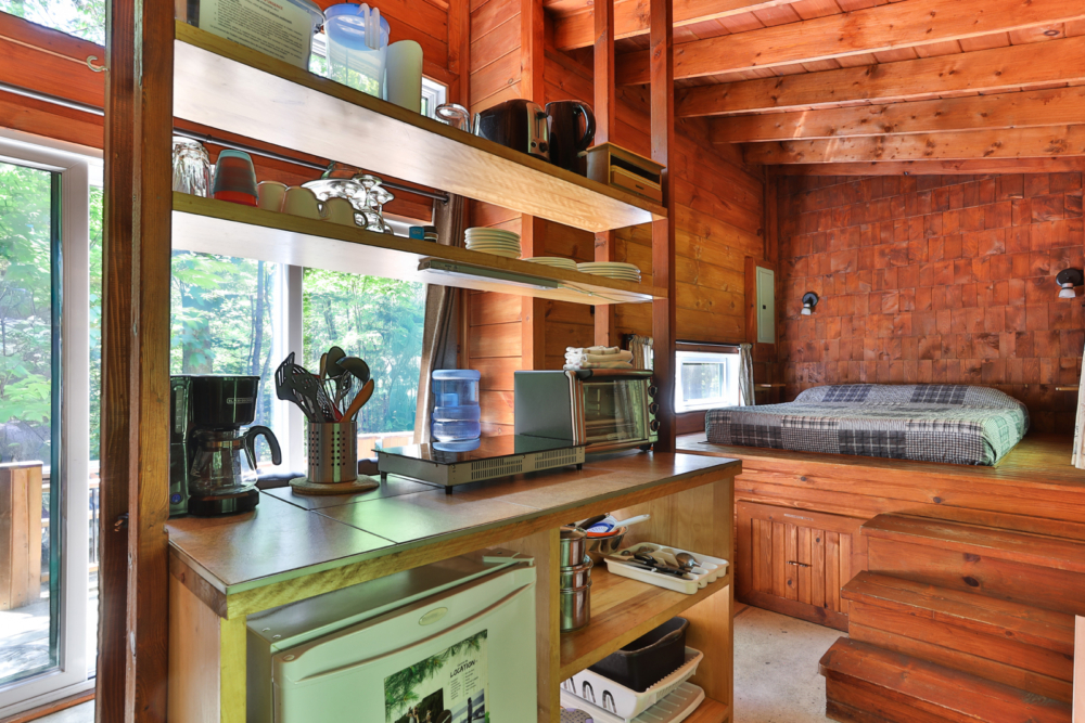 Cuisine équipée dans l’intérieur chaleureux d’une cabane, avec machine à café, grille-pain, réfrigérateur et coin repas.