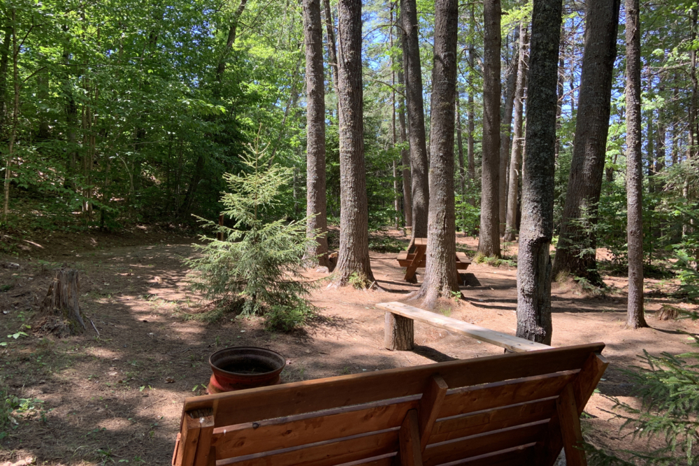 Wooden outdoor seating and a fire pit in a peaceful forest campsite at Chalets Lanaudière.