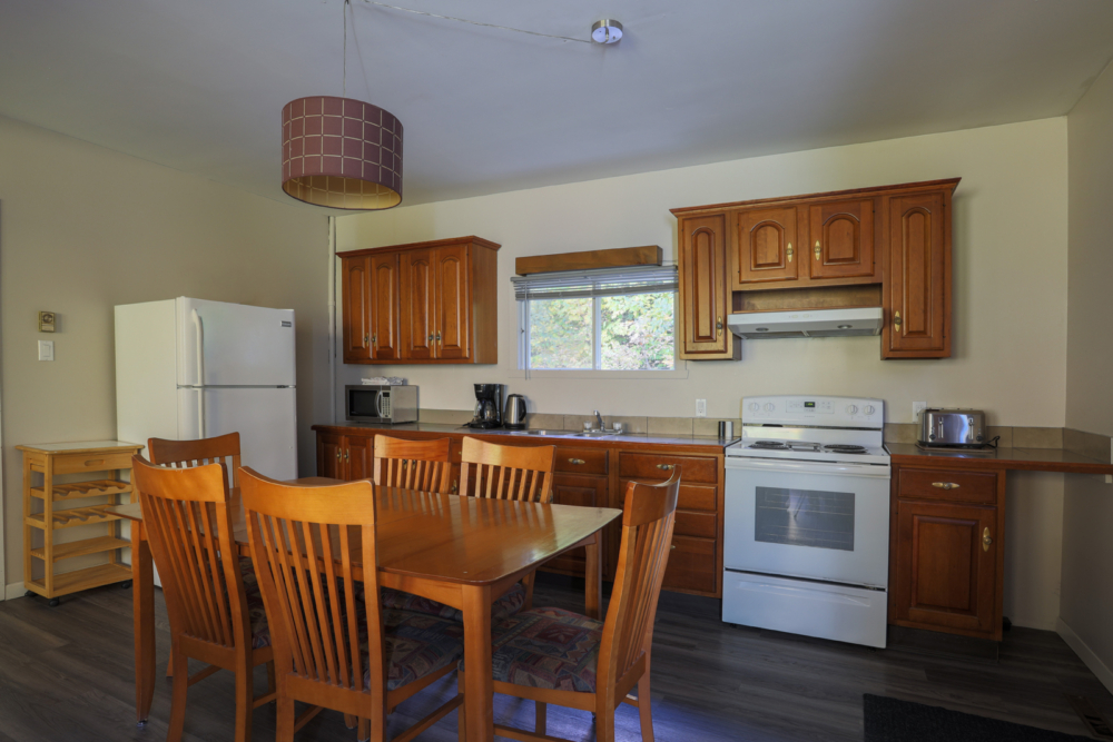 Cuisine entièrement équipée d’un chalet, avec table à manger en bois, réfrigérateur, cuisinière et armoires en bois.