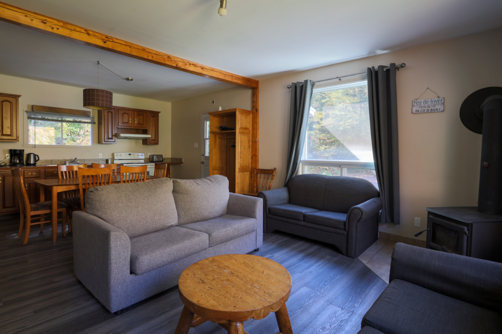 Intérieur chaleureux d’un chalet avec salon, cuisine, coin repas et poêle à bois.
