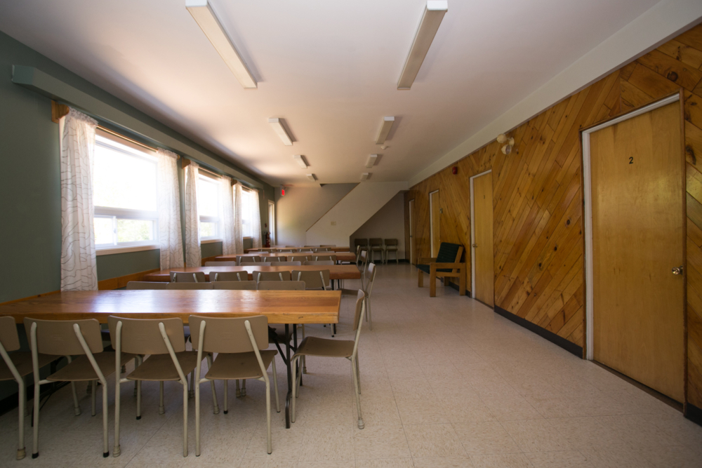 Salle à manger d'un chalet avec tables, chaises, fenêtres et portes en bois.