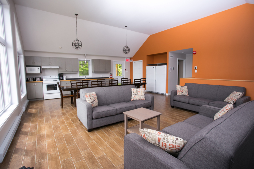 Intérieur chaleureux d’un chalet avec salon, trois canapés, cuisine moderne et grande fenestration.