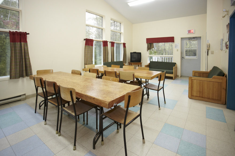 Salle à manger d’un chalet, avec murs clairs, grandes tables et grandes fenêtres.