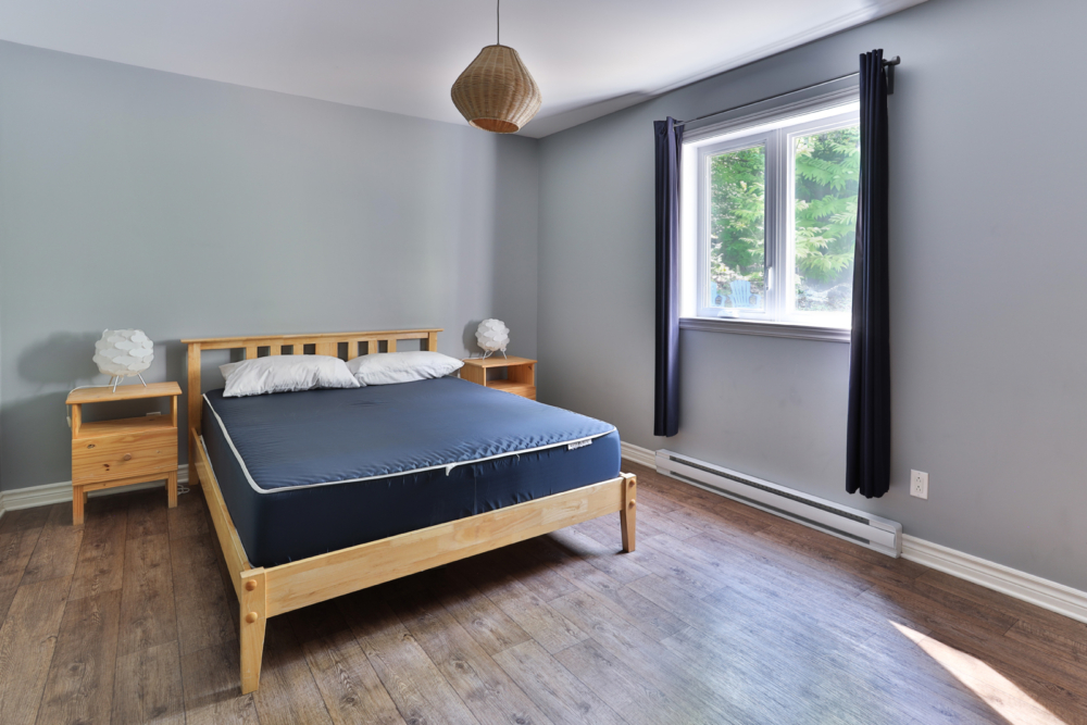 Chambre d'un chalet avec lit queen, tables de chevet et fenêtres avec vue sur la forêt.