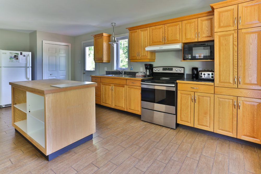 Cuisine entièrement équipée d’un chalet avec armoires en bois, îlot central, cuisinière, réfrigérateur et micro-ondes.