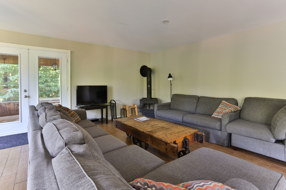 Salon chaleureux d’un chalet avec divans gris, poêle à bois, téléviseur et table basse rustique.