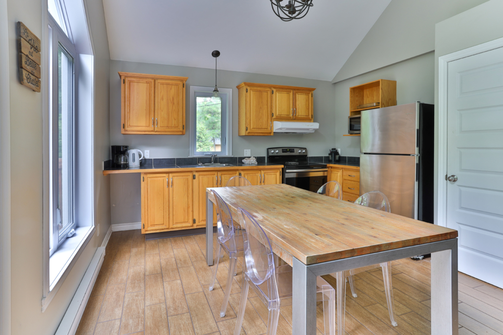 Cuisine armoires en bois et salle à manger d’un chalet, avec grande table en bois et électroménagers en acier inoxydable.