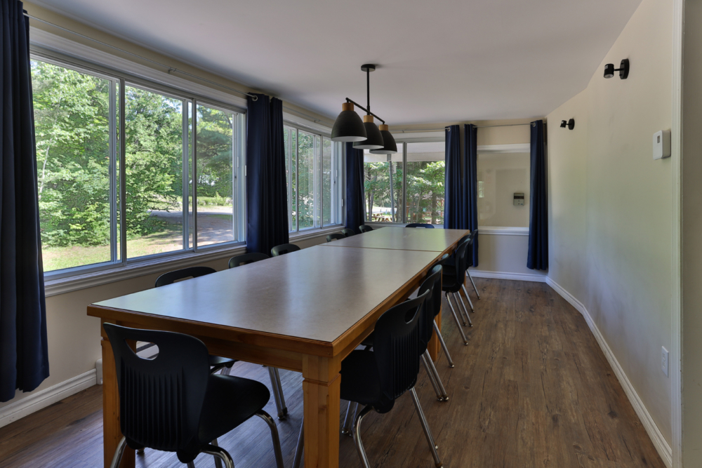 Salle à manger spacieuse d’un chalet, avec grande table en bois, chaises noires et fenêtres donnant sur la nature.