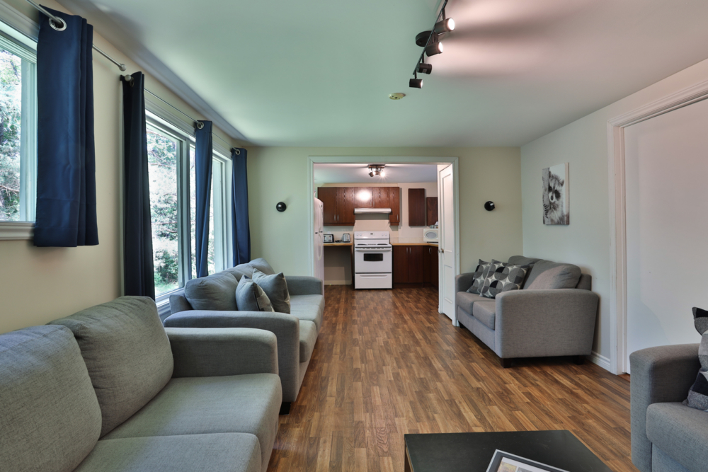 Salon spacieux et chaleureux d’un chalet, avec canapés, grandes fenêtres et cuisine entièrement équipée.