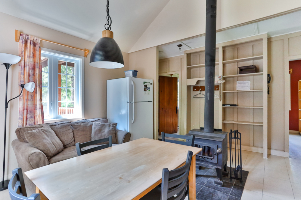 Intérieur chaleureux d’un chalet, avec cuisine, table à manger, canapé et poêle à bois.