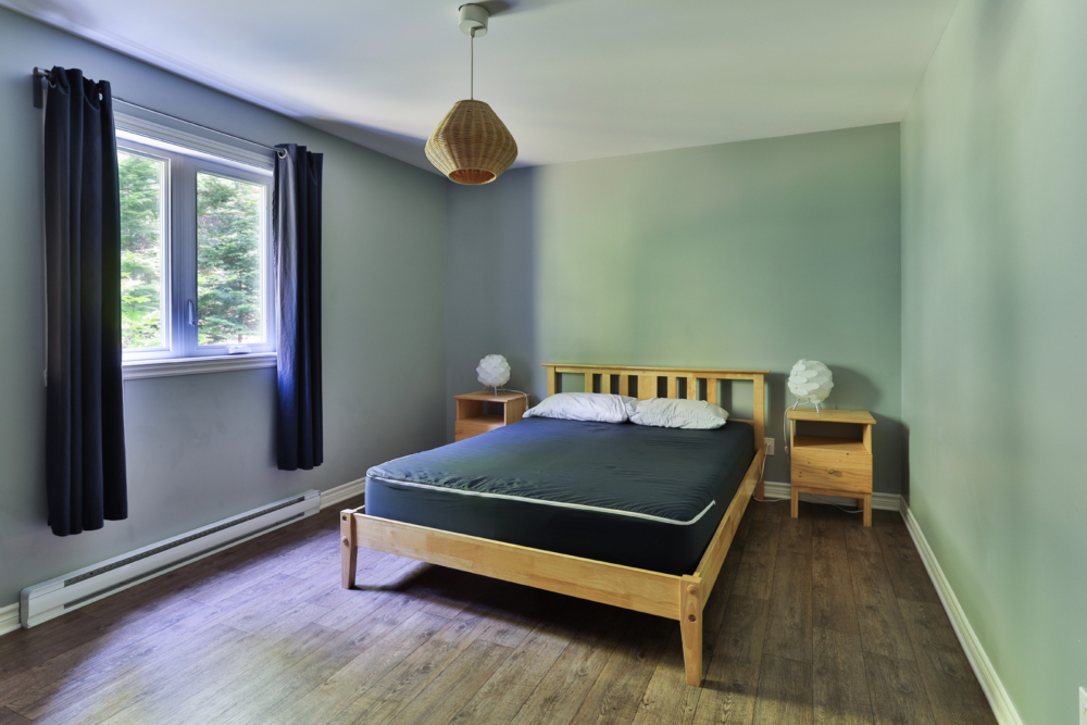 Chambre confortable d’un chalet avec lit en bois, tables de chevet et fenêtre donnant sur la nature.