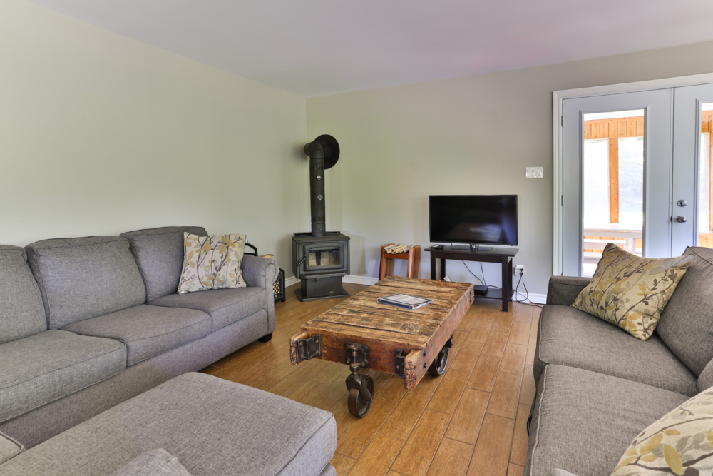 Salon chaleureux d’un chalet avec canapés, poêle à bois, téléviseur et table basse en bois.