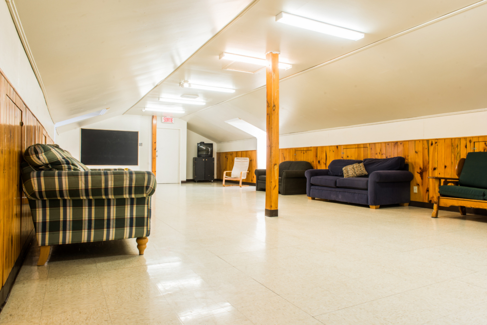 Salon commun d’un chalet avec fauteuils, canapés, télévision et murs lambrissés en bois.