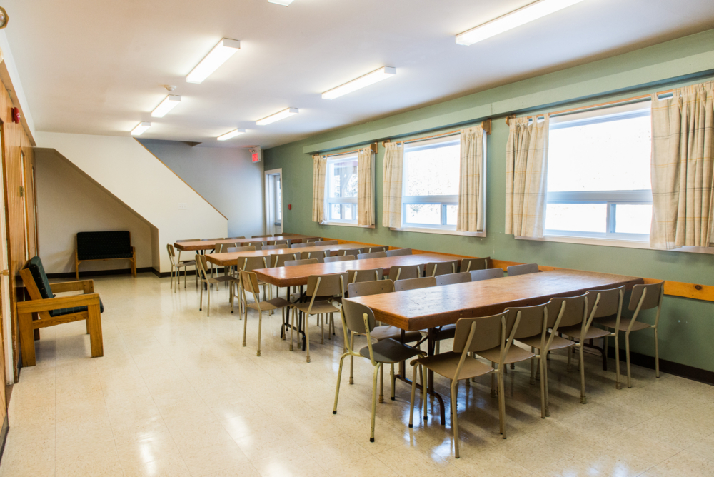 Salle à manger d’un chalet avec longues tables, chaises, fenêtres et bancs.
