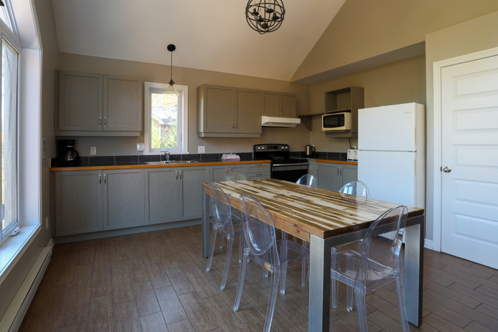 Cuisine moderne et lumineuse d’un chalet avec table en bois, électroménagers et chaises transparentes.