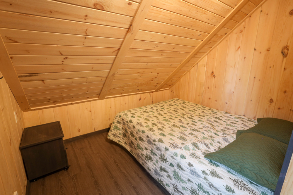Chambre douillette d’un mini-chalet avec lit double, murs et plafond en bois.
