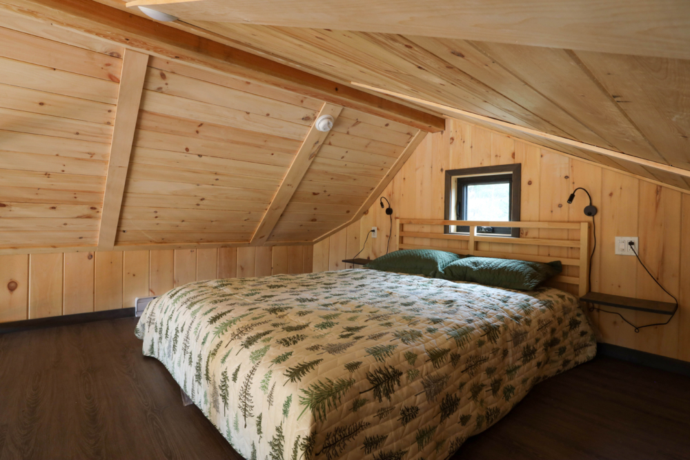 Chambre douillette d’un mini-chalet avec lit double, literie à motifs d'arbres et murs en bois.
