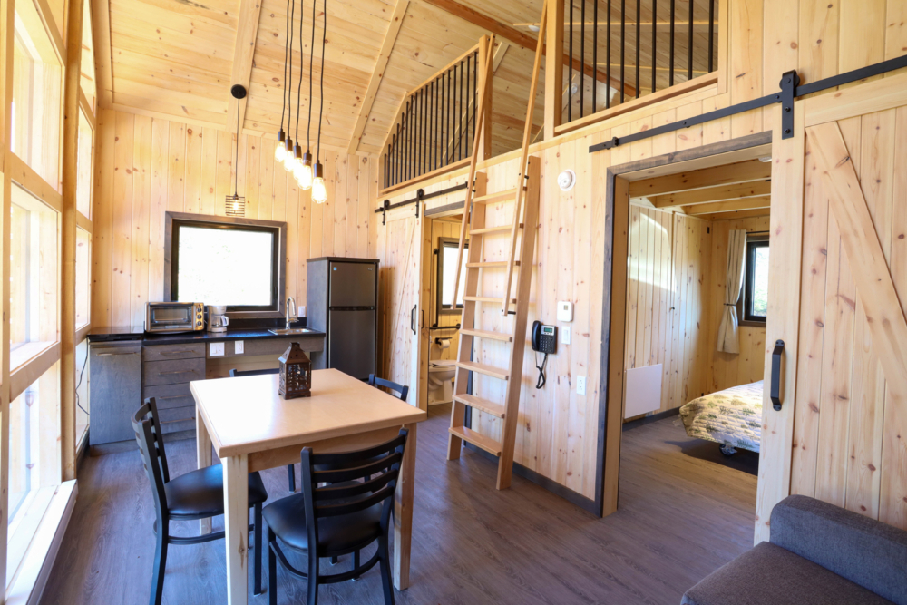 Intérieur chaleureux d’un mini-chalet avec cuisine, coin repas, mezzanine et chambre.