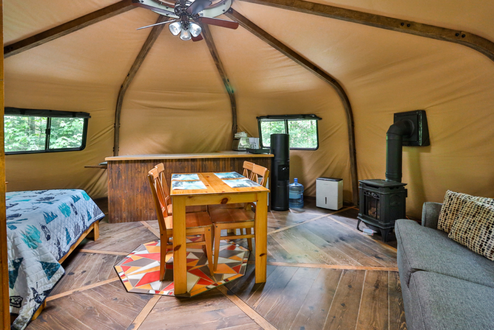 Intérieur chaleureux d’une yourte avec lits, table à manger, divan et poêle à bois.
