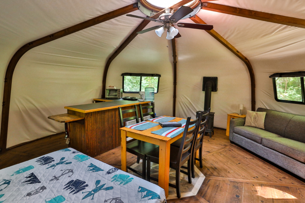 Intérieur d’une yourte style glamping avec cuisine, salle à manger, divan-lit et chambre.