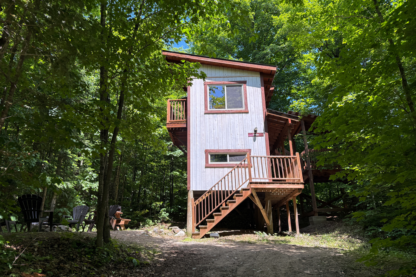 Cabane en bois niché en forêt, avec escalier extérieur, balcon et aire de détente.