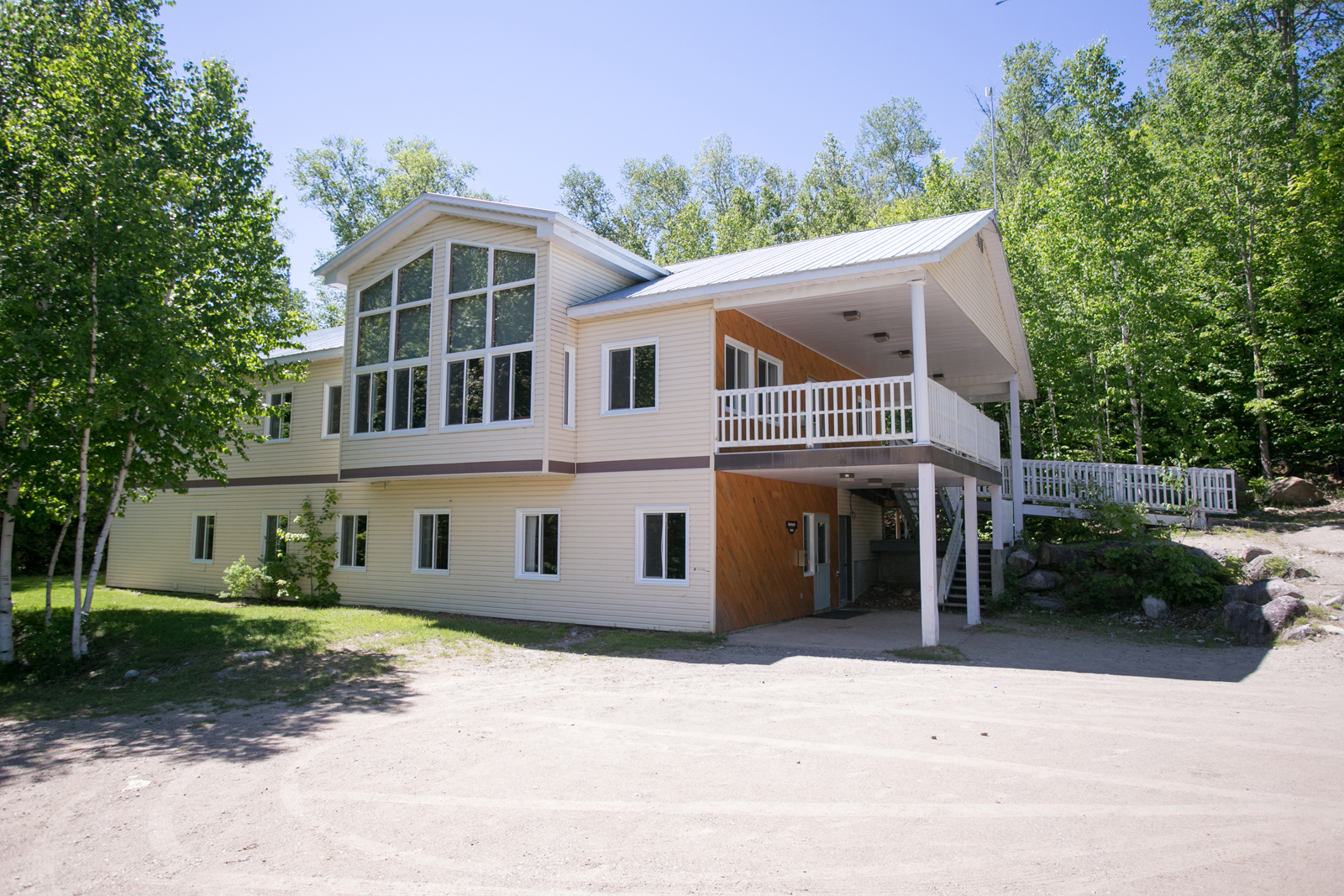 Chalet à deux étages avec grande fenestration et terrasse couverte, entouré d’arbres.