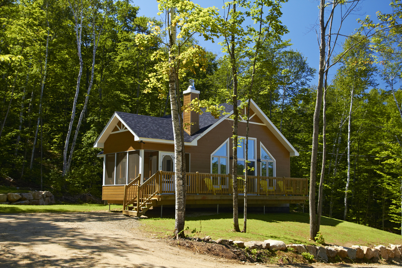 Chalet entouré d’arbres, avec grande terrasse en bois et grandes fenêtres.