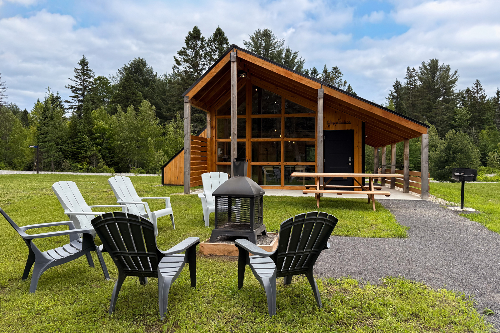 Mini-chalet en bois avec terrasse, foyer extérieur, mobilier Adirondack en forêt.