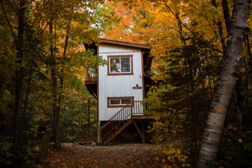 Petit chalet perché dans les arbres, entouré d’une forêt aux couleurs automnales chez Chalets Lanaudière.