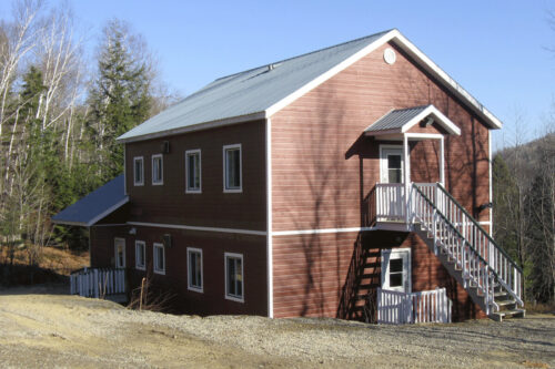 Chalet entouré d’arbres, avec escalier extérieur et grandes fenêtres.