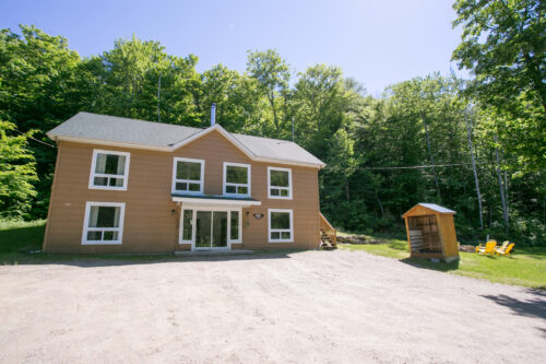 Chalet entouré d’arbres, muni de plusieurs grandes fenêtres.