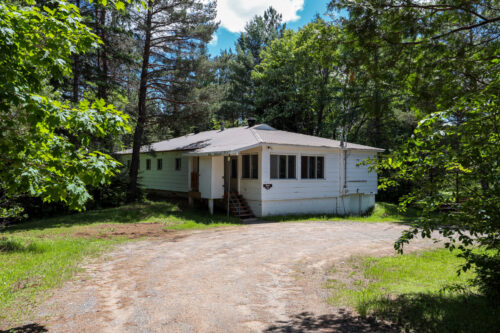 Chalet blanc entouré d’arbres, avec entrée accessible par une allée en gravier.
