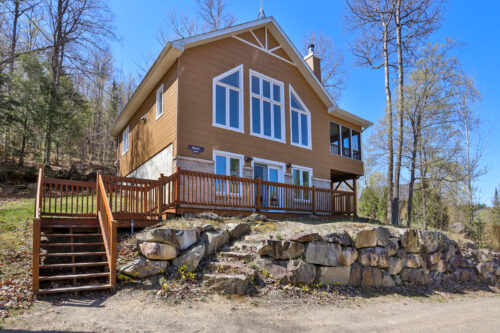 Chalet entouré d’arbres, avec terrasse, balcon et escalier menant à l’entrée.