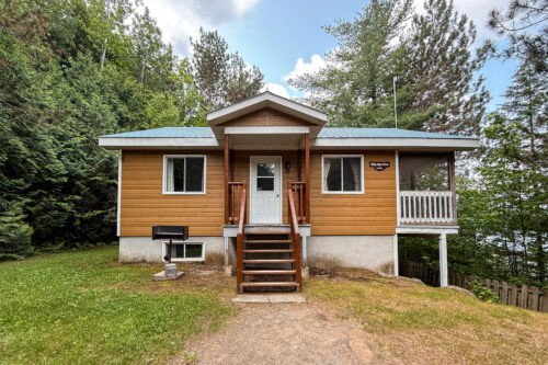 Chalet entouré d’arbres, avec balcon couvert et escalier menant à l’entrée.